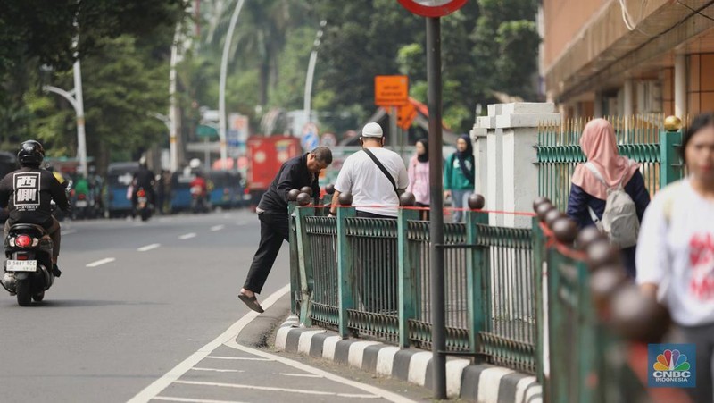 Sejumlah warga calon penumpang commuterline melompati pagar pembatas antara jalan dan Stasiun Cikini di Jakarta, Jumat (18/7/2025). (CNBC Indonesia/Tri Susilo)