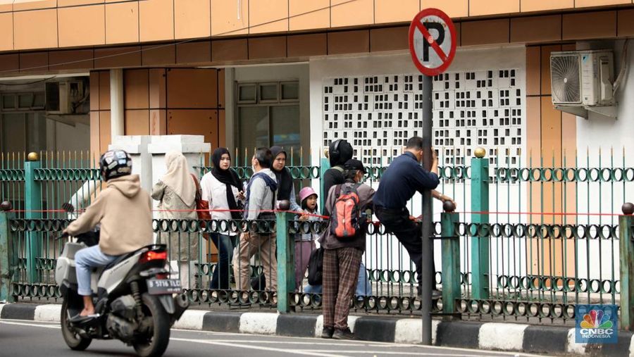 Sejumlah warga calon penumpang commuterline melompati pagar pembatas antara jalan dan Stasiun Cikini di Jakarta, Jumat (18/7/2025). (CNBC Indonesia/Tri Susilo)