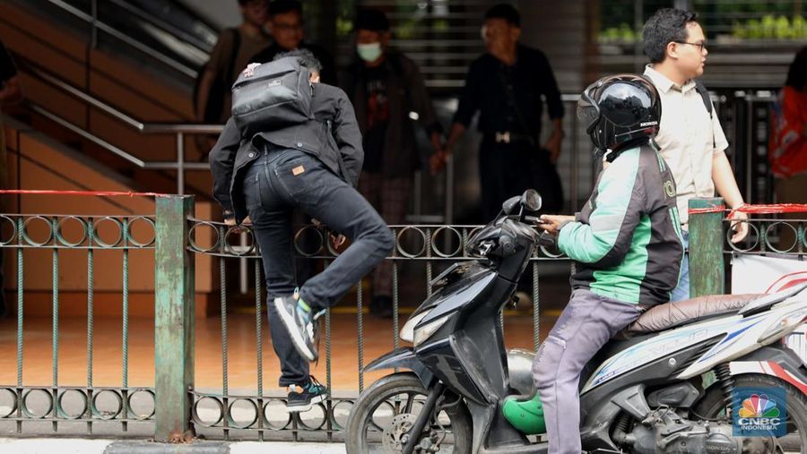 Sejumlah warga calon penumpang commuterline melompati pagar pembatas antara jalan dan Stasiun Cikini di Jakarta, Jumat (18/7/2025). (CNBC Indonesia/Tri Susilo)