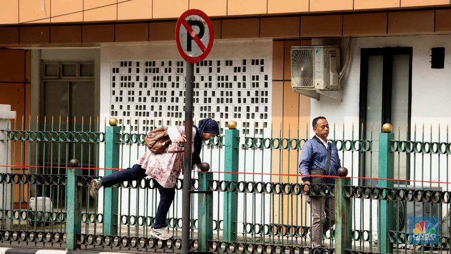 Sejumlah warga calon penumpang commuterline melompati pagar pembatas antara jalan dan Stasiun Cikini di Jakarta, Jumat (18/7/2025). (CNBC Indonesia/Tri Susilo)