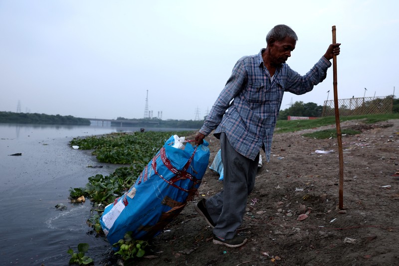 Ramu Gupta, seorang pria berusia 67 tahun yang pergi ke sungai untuk berburu koin dan barang berharga lainnya, mengeluarkan tas berisi plastik dari perairan sungai Yamuna di New Delhi, India, 26 Juni 2025. (REUTERS/Bhawika Chhabra)
