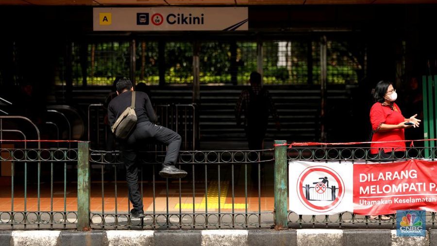 Sejumlah warga calon penumpang commuterline melompati pagar pembatas antara jalan dan Stasiun Cikini di Jakarta, Jumat (18/7/2025). (CNBC Indonesia/Tri Susilo)