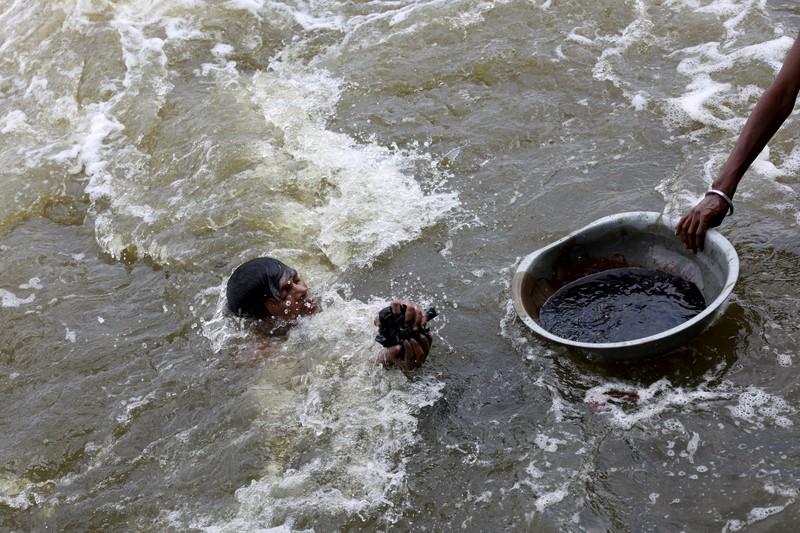 Ramu Gupta, seorang pria berusia 67 tahun yang pergi ke sungai untuk berburu koin dan barang berharga lainnya, mengeluarkan tas berisi plastik dari perairan sungai Yamuna di New Delhi, India, 26 Juni 2025. (REUTERS/Bhawika Chhabra)