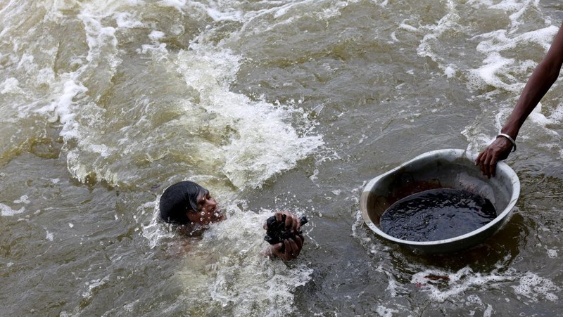 Ramu Gupta, seorang pria berusia 67 tahun yang pergi ke sungai untuk berburu koin dan barang berharga lainnya, mengeluarkan tas berisi plastik dari perairan sungai Yamuna di New Delhi, India, 26 Juni 2025. (REUTERS/Bhawika Chhabra)