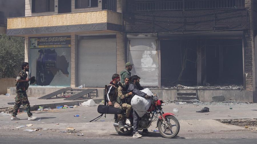 Pejuang Badui berjalan di sepanjang jalan sambil memegang senjata mereka di Sweida, Suriah, Sabtu (19/7/2025). (REUTERS/Karam al-Masri)