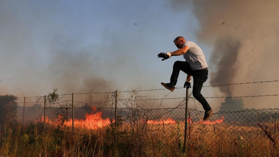 Seseorang berdiri di tengah asap saat kebakaran hutan melanda sebuah desa di Dubrava, Kosovo, 22 Juli 2025. (REUTERS/Valdrin Xhemaj)