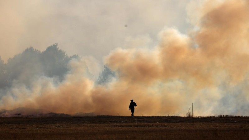 Seseorang berdiri di tengah asap saat kebakaran hutan melanda sebuah desa di Dubrava, Kosovo, 22 Juli 2025. (REUTERS/Valdrin Xhemaj)