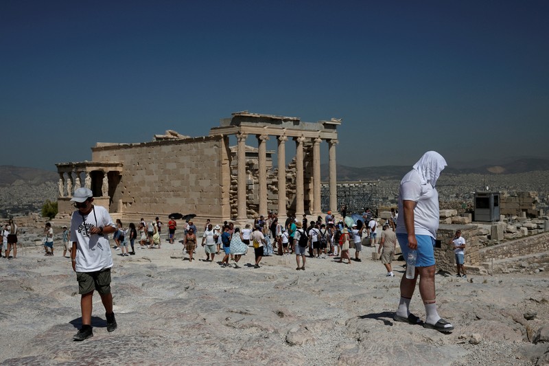 Orang-orang berjalan di depan kuil Erechtheion di puncak bukit Acropolis saat gelombang panas melanda dengan suhu diperkirakan mencapai 40 derajat Celsius, di Athena, Yunani, 24 Juli 2025. (REUTERS/Louiza Vradi)