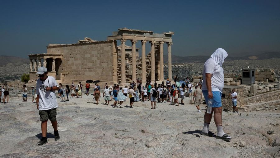 Orang-orang berjalan di depan kuil Erechtheion di puncak bukit Acropolis saat gelombang panas melanda dengan suhu diperkirakan mencapai 40 derajat Celsius, di Athena, Yunani, 24 Juli 2025. (REUTERS/Louiza Vradi)
