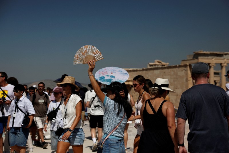 Orang-orang berjalan di depan kuil Erechtheion di puncak bukit Acropolis saat gelombang panas melanda dengan suhu diperkirakan mencapai 40 derajat Celsius, di Athena, Yunani, 24 Juli 2025. (REUTERS/Louiza Vradi)