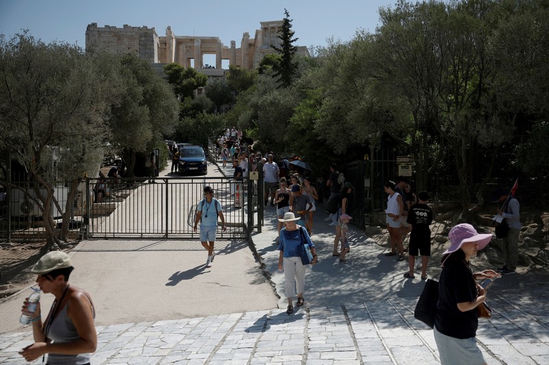 Orang-orang berjalan di depan kuil Erechtheion di puncak bukit Acropolis saat gelombang panas melanda dengan suhu diperkirakan mencapai 40 derajat Celsius, di Athena, Yunani, 24 Juli 2025. (REUTERS/Louiza Vradi)
