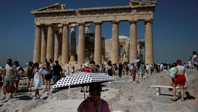 Orang-orang berjalan di depan kuil Erechtheion di puncak bukit Acropolis saat gelombang panas melanda dengan suhu diperkirakan mencapai 40 derajat Celsius, di Athena, Yunani, 24 Juli 2025. (REUTERS/Louiza Vradi)