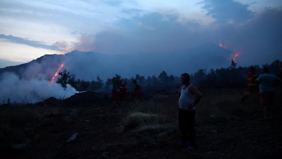 Seorang anggota layanan darurat berdiri di samping kebakaran hutan di dekat Bulqiza, Albania, Sabtu (26/7/2025). (REUTERS/Florion Goga)