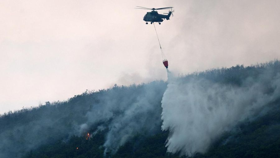 Seorang anggota layanan darurat berdiri di samping kebakaran hutan di dekat Bulqiza, Albania, Sabtu (26/7/2025). (REUTERS/Florion Goga)