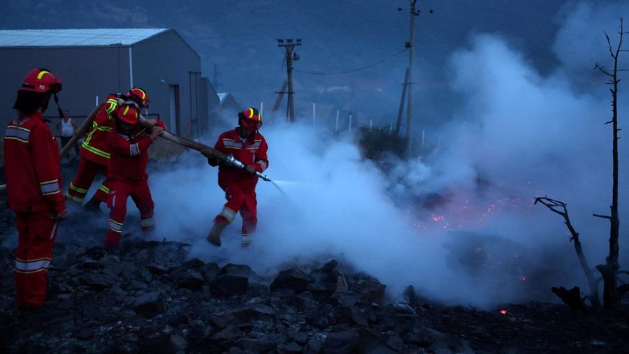 Seorang anggota layanan darurat berdiri di samping kebakaran hutan di dekat Bulqiza, Albania, Sabtu (26/7/2025). (REUTERS/Florion Goga)