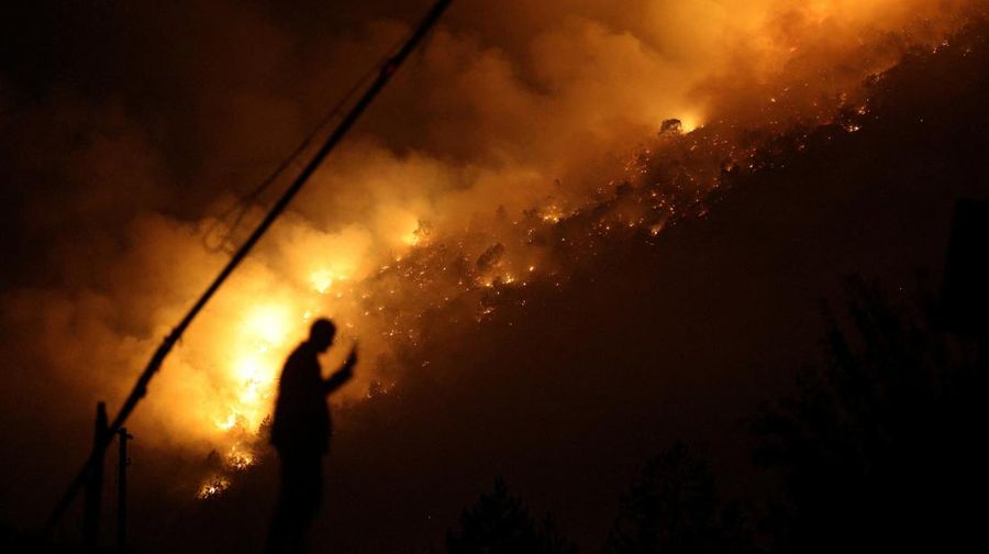 Seorang anggota layanan darurat berdiri di samping kebakaran hutan di dekat Bulqiza, Albania, Sabtu (26/7/2025). (REUTERS/Florion Goga)