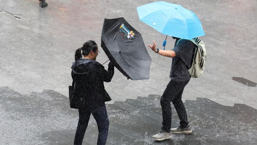 Orang-orang mencoba memperbaiki payung yang tertiup angin saat berjalan di jalan saat hujan deras dan angin kencang, setelah Badai Tropis Co-May mendarat di kota terdekat, di Shanghai, CHina, Rabu (30/7/2025). (REUTERS/Go Nakamura)