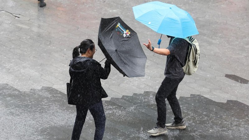 Orang-orang mencoba memperbaiki payung yang tertiup angin saat berjalan di jalan saat hujan deras dan angin kencang, setelah Badai Tropis Co-May mendarat di kota terdekat, di Shanghai, CHina, Rabu (30/7/2025). (REUTERS/Go Nakamura)