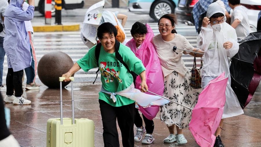 Orang-orang mencoba memperbaiki payung yang tertiup angin saat berjalan di jalan saat hujan deras dan angin kencang, setelah Badai Tropis Co-May mendarat di kota terdekat, di Shanghai, CHina, Rabu (30/7/2025). (REUTERS/Go Nakamura)