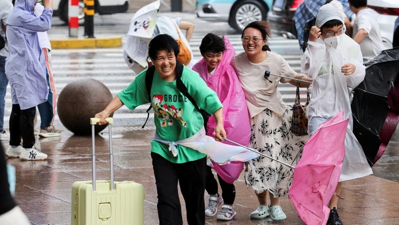 Orang-orang mencoba memperbaiki payung yang tertiup angin saat berjalan di jalan saat hujan deras dan angin kencang, setelah Badai Tropis Co-May mendarat di kota terdekat, di Shanghai, CHina, Rabu (30/7/2025). (REUTERS/Go Nakamura)