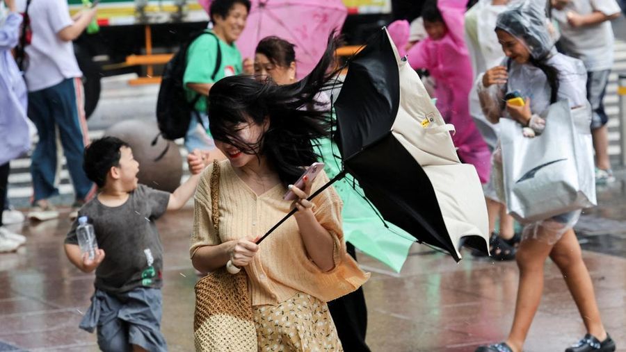 Orang-orang mencoba memperbaiki payung yang tertiup angin saat berjalan di jalan saat hujan deras dan angin kencang, setelah Badai Tropis Co-May mendarat di kota terdekat, di Shanghai, CHina, Rabu (30/7/2025). (REUTERS/Go Nakamura)
