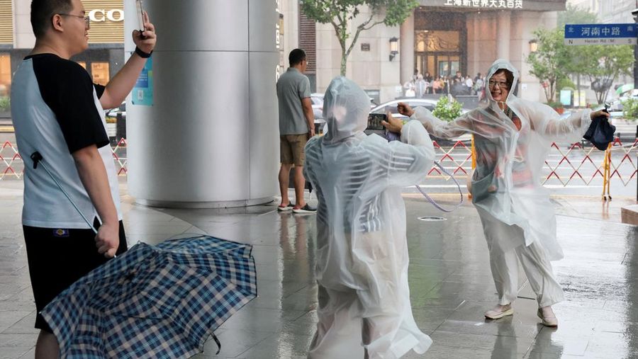 Orang-orang mencoba memperbaiki payung yang tertiup angin saat berjalan di jalan saat hujan deras dan angin kencang, setelah Badai Tropis Co-May mendarat di kota terdekat, di Shanghai, CHina, Rabu (30/7/2025). (REUTERS/Go Nakamura)