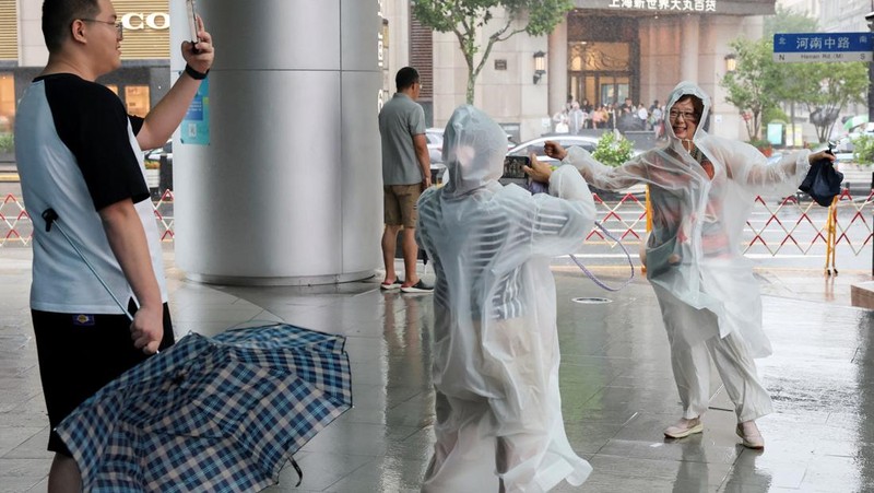 Orang-orang mencoba memperbaiki payung yang tertiup angin saat berjalan di jalan saat hujan deras dan angin kencang, setelah Badai Tropis Co-May mendarat di kota terdekat, di Shanghai, CHina, Rabu (30/7/2025). (REUTERS/Go Nakamura)