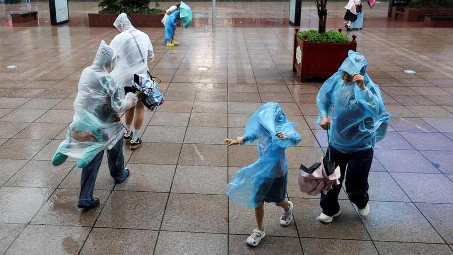 Orang-orang mencoba memperbaiki payung yang tertiup angin saat berjalan di jalan saat hujan deras dan angin kencang, setelah Badai Tropis Co-May mendarat di kota terdekat, di Shanghai, CHina, Rabu (30/7/2025). (REUTERS/Go Nakamura)