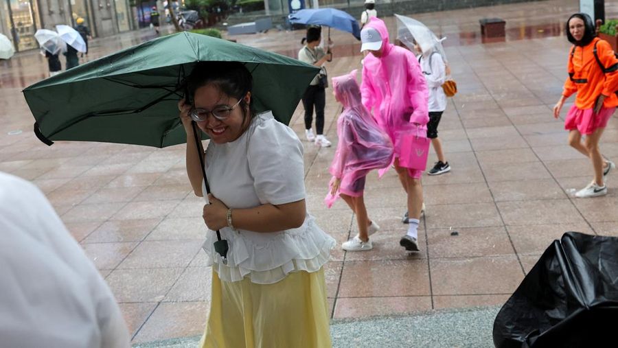 Orang-orang mencoba memperbaiki payung yang tertiup angin saat berjalan di jalan saat hujan deras dan angin kencang, setelah Badai Tropis Co-May mendarat di kota terdekat, di Shanghai, CHina, Rabu (30/7/2025). (REUTERS/Go Nakamura)