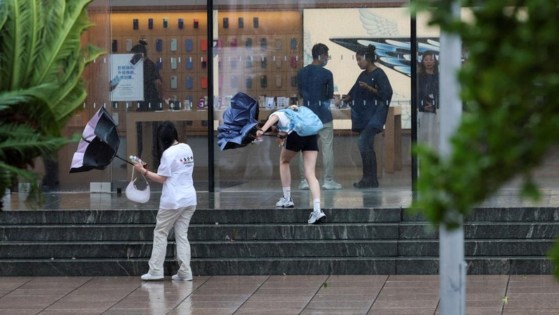 Orang-orang mencoba memperbaiki payung yang tertiup angin saat berjalan di jalan saat hujan deras dan angin kencang, setelah Badai Tropis Co-May mendarat di kota terdekat, di Shanghai, CHina, Rabu (30/7/2025). (REUTERS/Go Nakamura)