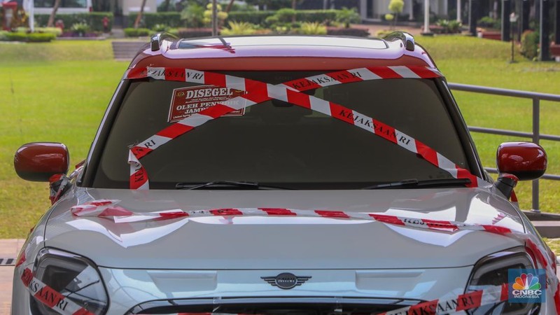 Petugas melihat mobil sitaan milik raja minyak Riza Chalid yang terparkir di Gedung Jampidsus, Kejaksaan Agung (Kejagung), Jakarta, Selasa (5/8/2025). (CNBC Indonesia/Faisal Rahman)
