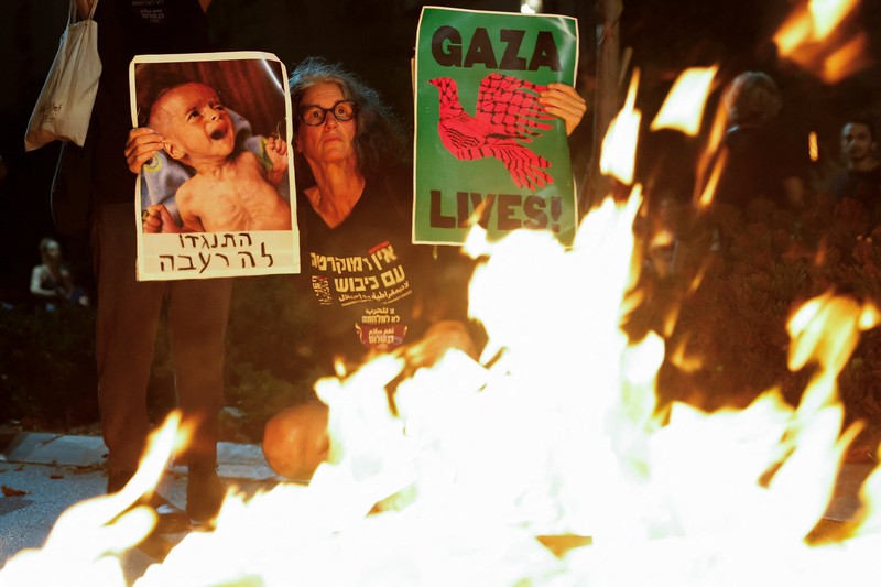 Demonstrators and relatives of hostages kidnapped during the deadly October 7, 2023, attack on Israel by Hamas, protest demanding the immediate release of the hostages and the end of the war, as a fire burns in Tel Aviv, Israel, August 7, 2025. REUTERS/Ammar Awad
