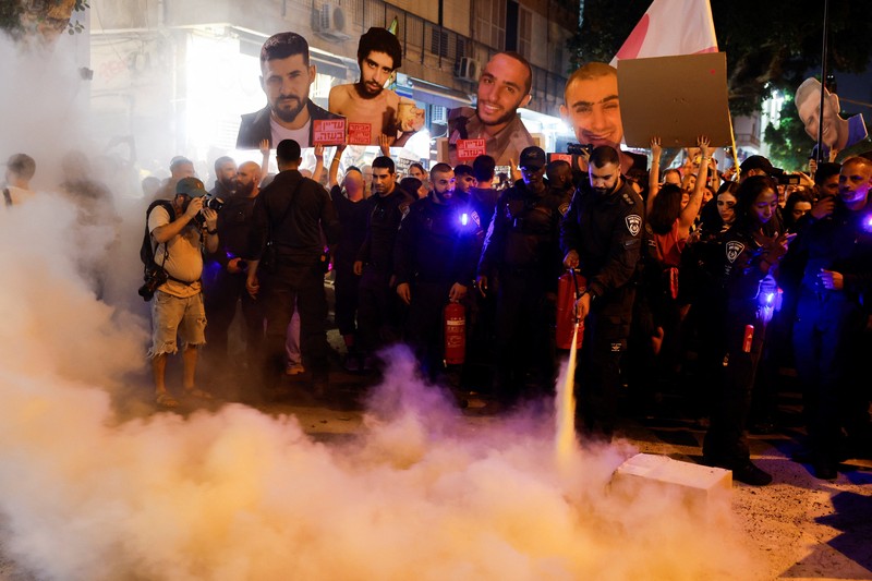 Demonstrators and relatives of hostages kidnapped during the deadly October 7, 2023, attack on Israel by Hamas, protest demanding the immediate release of the hostages and the end of the war, as a fire burns in Tel Aviv, Israel, August 7, 2025. REUTERS/Ammar Awad