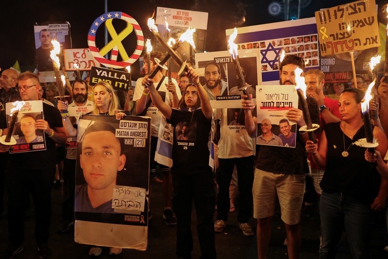Demonstrators and relatives of hostages kidnapped during the deadly October 7, 2023, attack on Israel by Hamas, protest demanding the immediate release of the hostages and the end of the war, as a fire burns in Tel Aviv, Israel, August 7, 2025. REUTERS/Ammar Awad