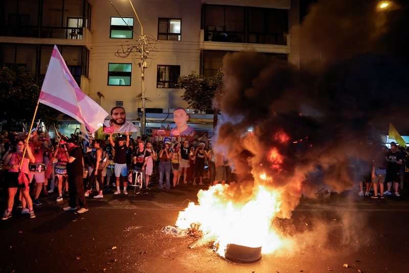Demonstrators and relatives of hostages kidnapped during the deadly October 7, 2023, attack on Israel by Hamas, protest demanding the immediate release of the hostages and the end of the war, as a fire burns in Tel Aviv, Israel, August 7, 2025. REUTERS/Ammar Awad
