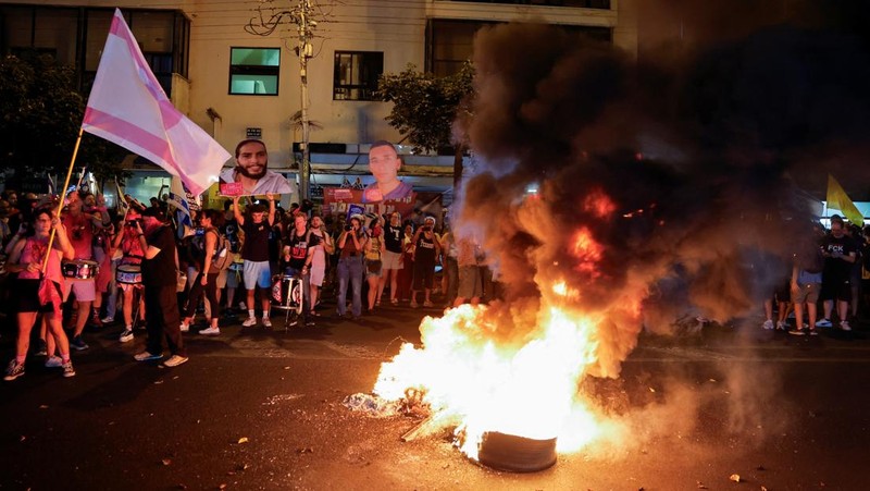 Demonstrators and relatives of hostages kidnapped during the deadly October 7, 2023, attack on Israel by Hamas, protest demanding the immediate release of the hostages and the end of the war, as a fire burns in Tel Aviv, Israel, August 7, 2025. REUTERS/Ammar Awad
