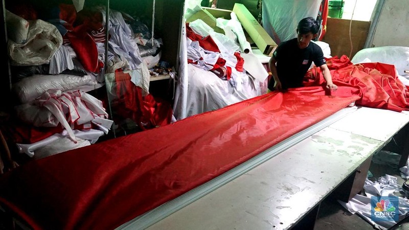 Pekerja melipat bendera di usaha konveksi rumahan yang memproduksi bendera umbul-umbul merah putih, topi, hingga kaos di kawasan Tangerang Selatan, Banten, Senin (11/8/2025). (CNBC Indonesia/Muhammad Sabki)