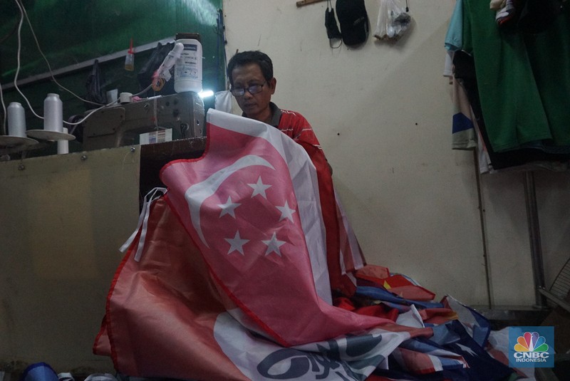 Pekerja melipat bendera di usaha konveksi rumahan yang memproduksi bendera umbul-umbul merah putih, topi, hingga kaos di kawasan Tangerang Selatan, Banten, Senin (11/8/2025). (CNBC Indonesia/Muhammad Sabki)