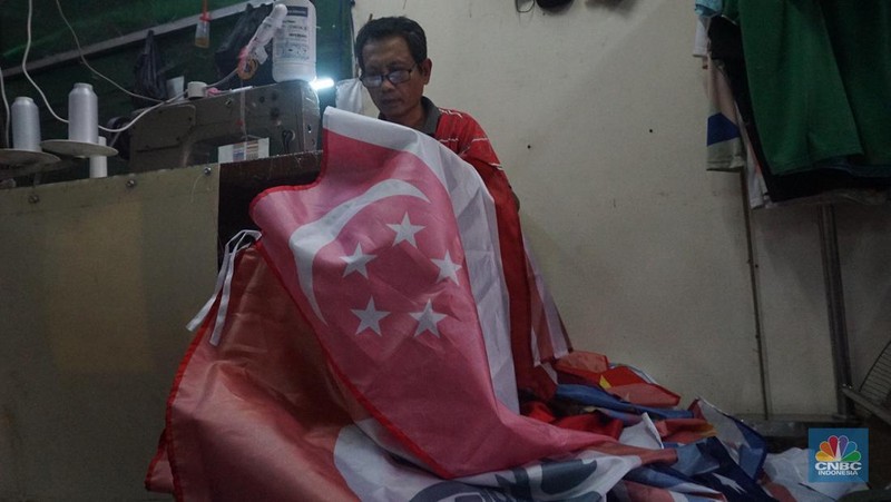 Pekerja melipat bendera di usaha konveksi rumahan yang memproduksi bendera umbul-umbul merah putih, topi, hingga kaos di kawasan Tangerang Selatan, Banten, Senin (11/8/2025). (CNBC Indonesia/Muhammad Sabki)