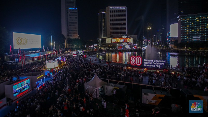 Warga menyaksikan iring-iringan karnaval saat melintas di kawasan Bundaran HI, Jakarta, Minggu (17/8/2025) malam. Acara karnaval ini menjadi pertama kalinya digelar pihak Istana dalam peringatan HUT RI. (CNBC Indonesia/Faisal Rahman)