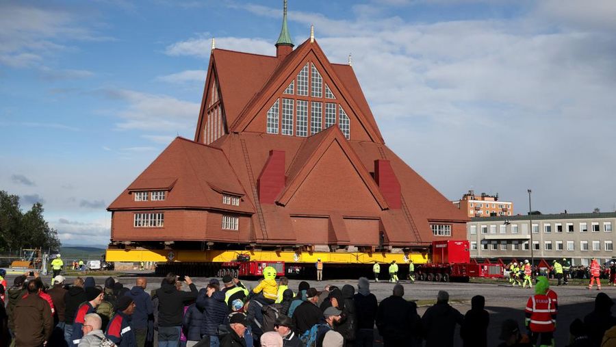 Orang-orang menggunakan ponsel mereka saat gereja kayu tua Kiruna dipindahkan selama perjalanan relokasi dua hari ke lokasi baru di sebelah pemakaman, untuk menyelamatkan dinding kayunya dari penurunan tanah dan perluasan tambang bijih besi bawah tanah terbesar di dunia, di Kiruna, Swedia 19 Agustus 2025. (REUTERS/Leonhard Foeger)|