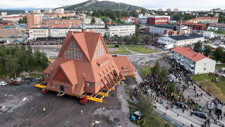Orang-orang menggunakan ponsel mereka saat gereja kayu tua Kiruna dipindahkan selama perjalanan relokasi dua hari ke lokasi baru di sebelah pemakaman, untuk menyelamatkan dinding kayunya dari penurunan tanah dan perluasan tambang bijih besi bawah tanah terbesar di dunia, di Kiruna, Swedia 19 Agustus 2025. (REUTERS/Leonhard Foeger)|