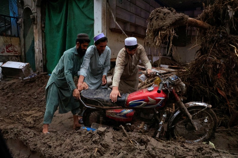 Para relawan berjalan sambil membawa payung untuk menghindari hujan saat mereka meninjau daerah yang rusak, menyusul badai yang menyebabkan hujan lebat dan banjir di Bayshonai Kalay, di distrik Buner, di provinsi Khyber Pakhtunkhwa, Pakistan, 18 Agustus 2025. (REUTERS/Akhtar Soomro)