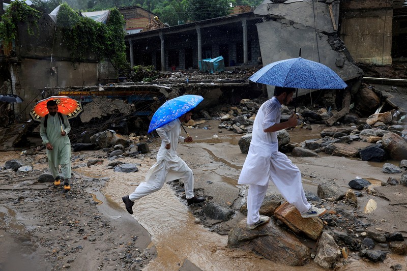 Para relawan berjalan sambil membawa payung untuk menghindari hujan saat mereka meninjau daerah yang rusak, menyusul badai yang menyebabkan hujan lebat dan banjir di Bayshonai Kalay, di distrik Buner, di provinsi Khyber Pakhtunkhwa, Pakistan, 18 Agustus 2025. (REUTERS/Akhtar Soomro)