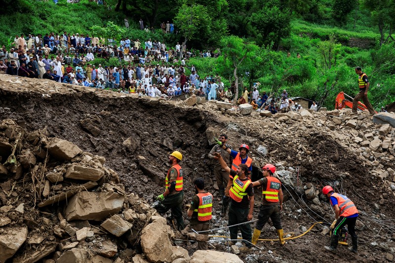 Para relawan berjalan sambil membawa payung untuk menghindari hujan saat mereka meninjau daerah yang rusak, menyusul badai yang menyebabkan hujan lebat dan banjir di Bayshonai Kalay, di distrik Buner, di provinsi Khyber Pakhtunkhwa, Pakistan, 18 Agustus 2025. (REUTERS/Akhtar Soomro)