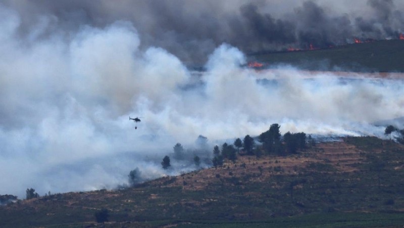 Asap mengepul saat helikopter terbang untuk memadamkan kebakaran hutan di pegunungan Oimbra, dekat Verin, di provinsi Ourense, wilayah Galicia, Spanyol, Selasa (19/8/2025). (REUTERS/Nacho Doce)