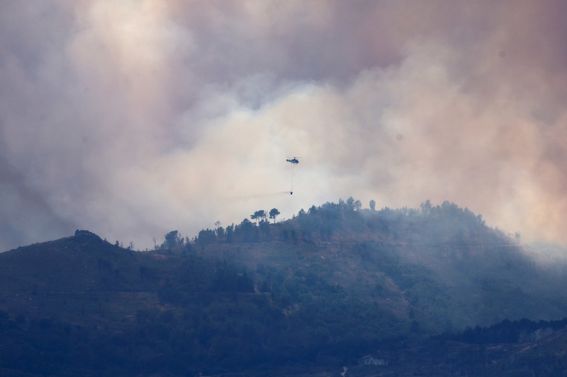 EUROPE-WEATHER/SPAIN-WILDFIRE Asap mengepul saat helikopter terbang untuk memadamkan kebakaran hutan di pegunungan Oimbra, dekat Verin, di provinsi Ourense, wilayah Galicia, Spanyol, Selasa (19/8/2025). (REUTERS/Nacho Doce)