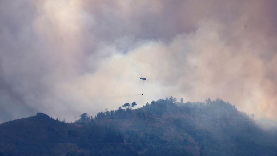 Asap mengepul saat helikopter terbang untuk memadamkan kebakaran hutan di pegunungan Oimbra, dekat Verin, di provinsi Ourense, wilayah Galicia, Spanyol, Selasa (19/8/2025). (REUTERS/Nacho Doce)