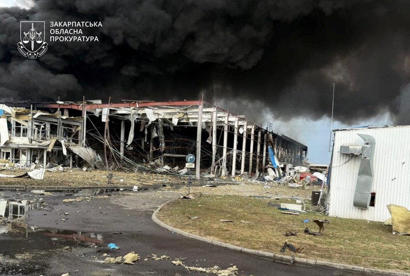 Personel penegak hukum menyaksikan asap mengepul di atas pabrik Flextronics yang terkena serangan rudal Rusia, di tengah serangan Rusia terhadap Ukraina, di Mukachevo, wilayah Zakarpattia, Ukraina, 21 Agustus 2025. (Zakarpattia Regional Prosecutor's Office/Handout via REUTERS)