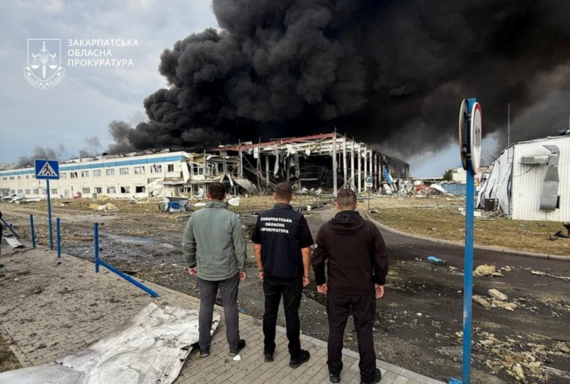 Personel penegak hukum menyaksikan asap mengepul di atas pabrik Flextronics yang terkena serangan rudal Rusia, di tengah serangan Rusia terhadap Ukraina, di Mukachevo, wilayah Zakarpattia, Ukraina, 21 Agustus 2025. (Zakarpattia Regional Prosecutor's Office/Handout via REUTERS)